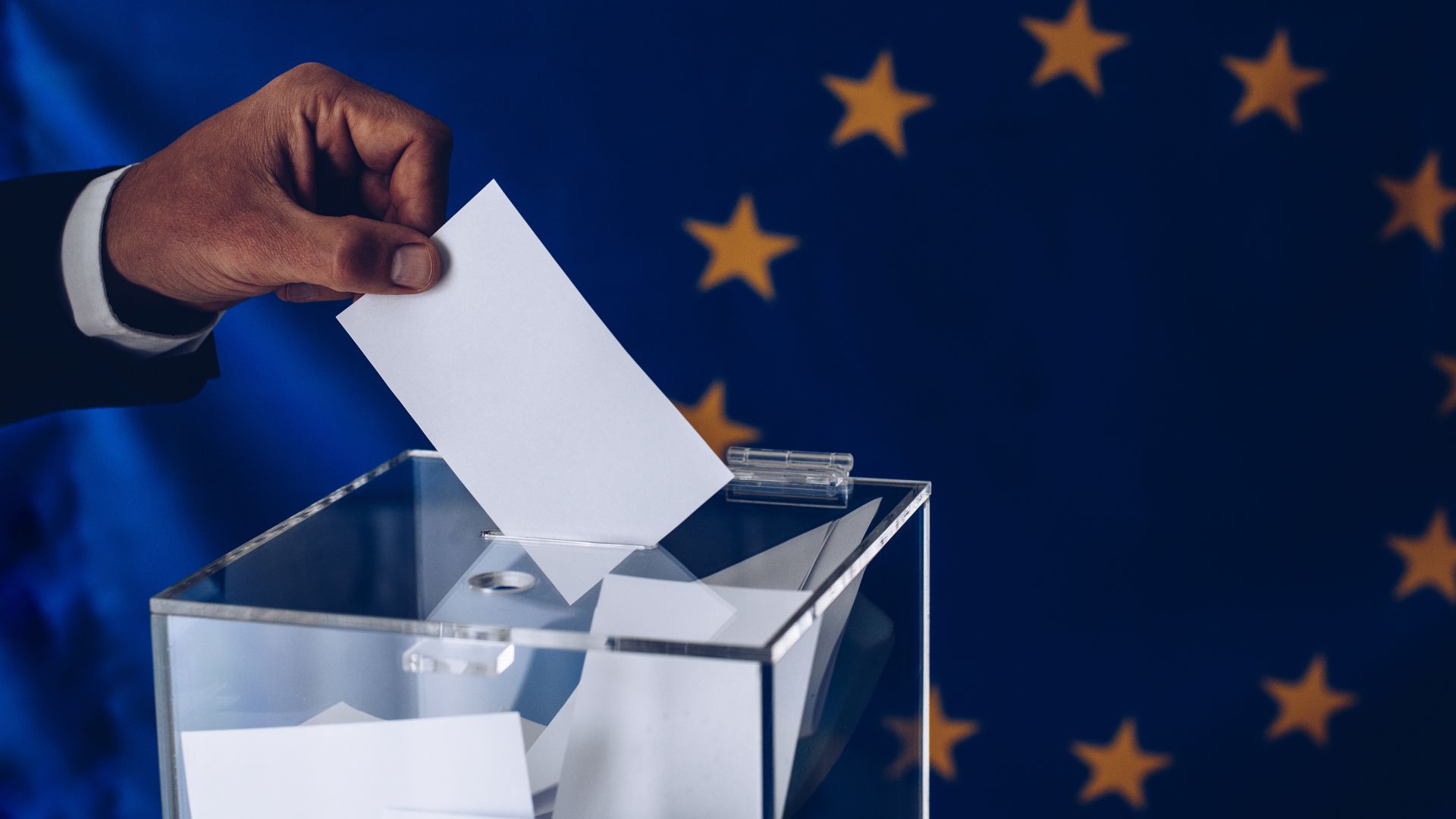 une main déposant un bulletin de vote avec le drapeau européen à l'arrière